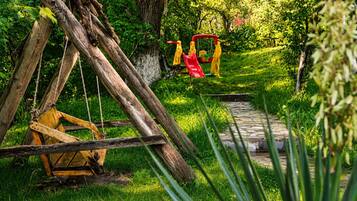 A rustic wooden swing set in a lush green garden with a stone pathway.