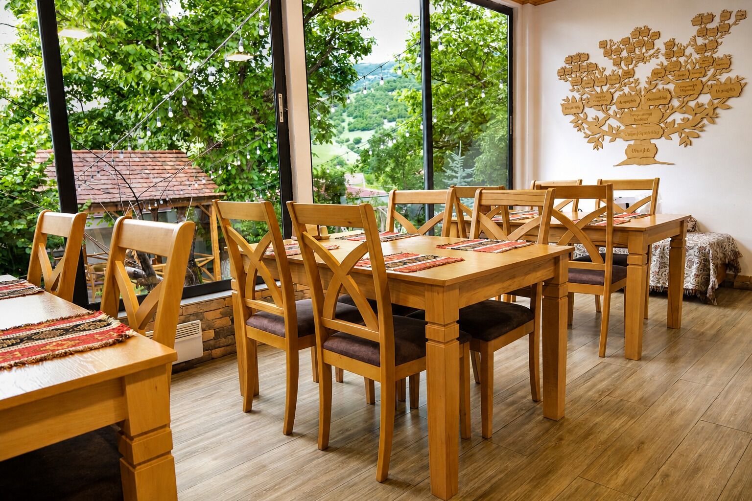 Un espace repas avec des tables et des chaises en bois, de grandes fenêtres donnant sur un paysage verdoyant et un schéma représentant un arbre, fixé au mur.