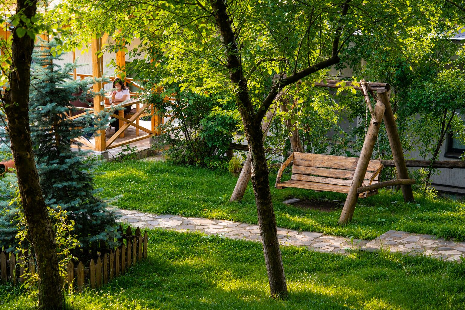Un’altalena di legno in un giardino rigoglioso con un vialetto in pietra.