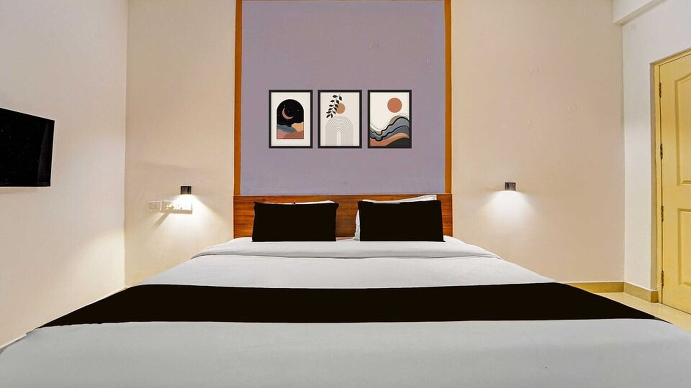 Ett hotellrum med en säng, två sänglampor och tre inramade konstverk på väggen.