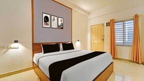 A hotel room with a bed, a nightstand, a wall-mounted lamp, a door, and a window with curtains.