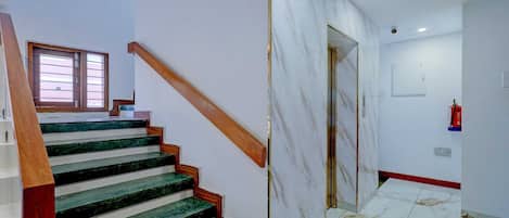 A staircase with green marble steps and wooden handrails, leading to a room with white walls and a tiled floor.