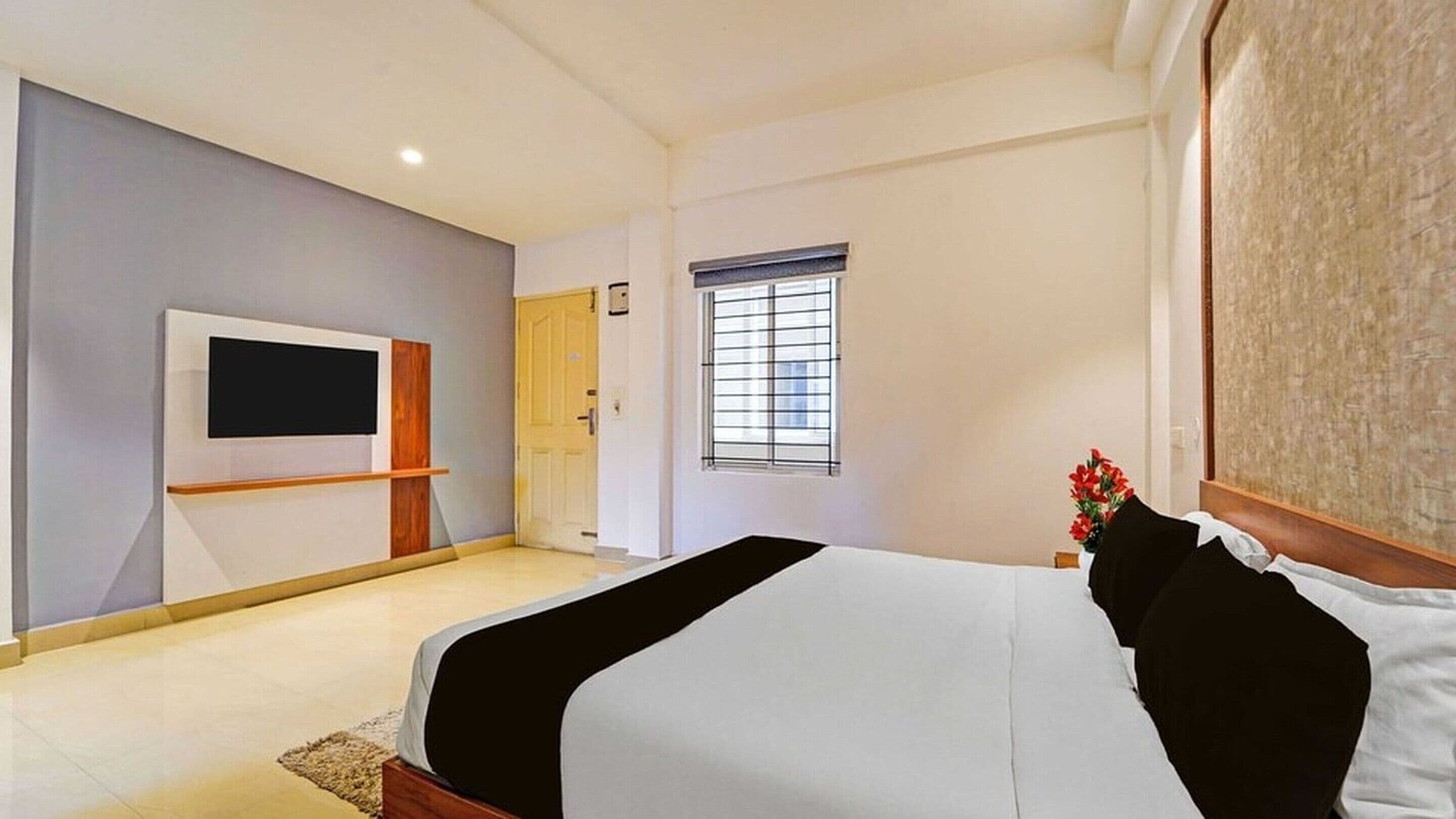 A hotel room with a bed, a TV mounted on the wall, a window with blinds, and a door.