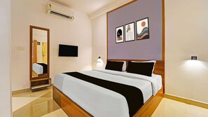 A hotel room with a bed, a flat-screen TV, an air conditioning unit, and artwork on the wall.