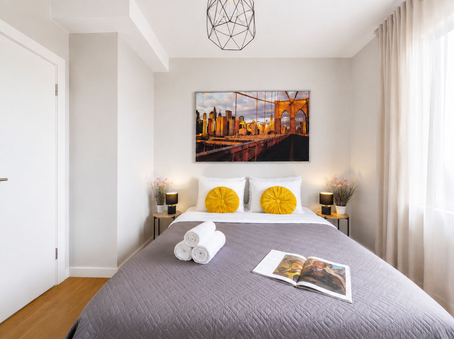 Een hotelkamer met een bed, een stadsgezicht schilderij, twee bedlampjes en een tijdschrift op het bed.