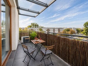 A balcony with a table and chairs, a view of the city, and a wooden fence. - Lumina 2BR Apart with Parking AC Balcony (Warszawa)