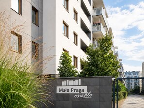A modern apartment building with balconies, a sign reading 'Mala Praha osiedle', and a gated entrance. - Lumina 2BR Apart with Parking AC Balcony (Warszawa)