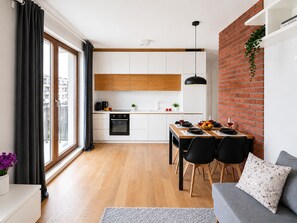 A modern kitchen with white cabinets, a black oven, and a dining area with a table set for two. - Lumina 2BR Apart with Parking AC Balcony (Warszawa)