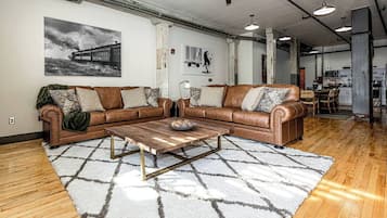 Ein geräumiger Wohnbereich mit einer großen braunen Ledersofa, einem Holztisch und einem gemusterten Teppich.