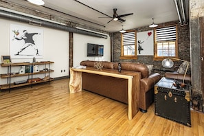 Ein modernes Wohnzimmer mit Holzboden, einem Ledersofa, einem Couchtisch und einem Vintage-Koffer.