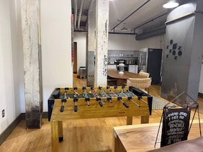 Ein Fußballtisch in einem Raum mit Holzboden, einer Kreidetafel und einer Küche im Hintergrund.