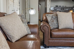 Zwei braune Ledersofas mit gemusterten Kissen, eine Stehlampe und eine Küche im Hintergrund.