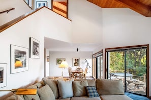 A spacious living area with a sofa, dining table, and chairs. There are framed pictures on the walls and a large window offering a view of the outdoors. - Caplan (TOT ID #2147): 3  BR, 2  BA House in The Sea Ranch, Sleeps 6 (The Sea Ranch)