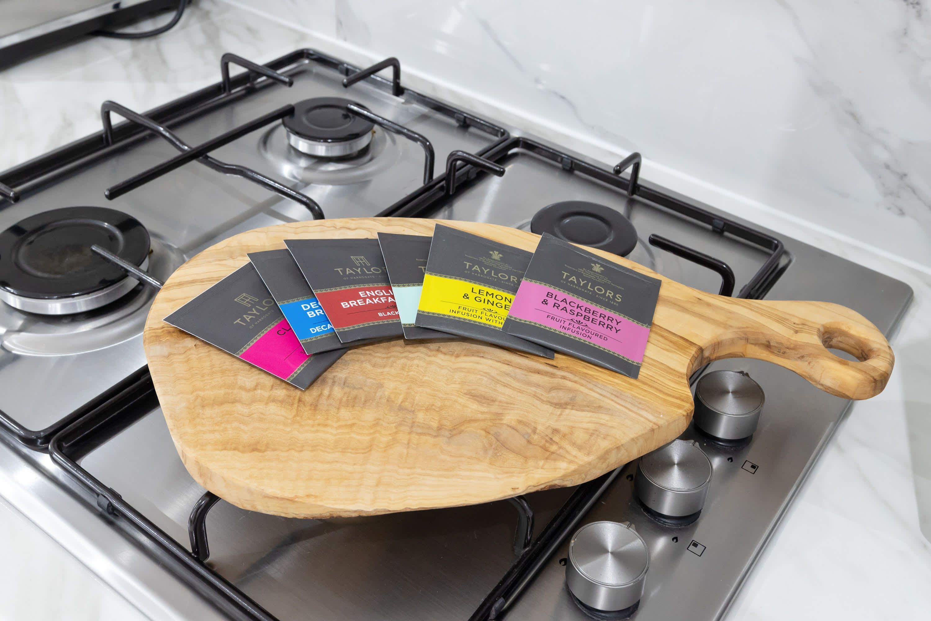 Une planche à découper en bois, sur laquelle sont apposées plusieurs étiquettes indiquant les différentes saveurs, posée sur une cuisinière à gaz.