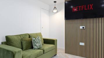 Een groene bank met een bloemenkussen, een Netflix-bord aan de muur en een wand van houten latten.