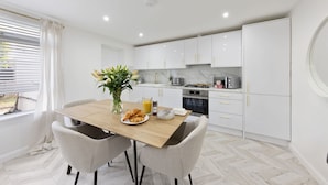 A modern kitchen with white cabinets, a wooden dining table, and two chairs. - Stylish Home Near Chelsfield Station Free Wifi (Orpington)
