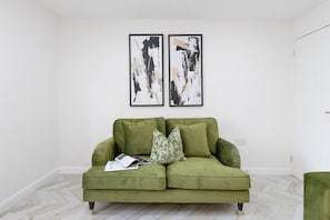 A green sofa with floral cushions, a magazine, and two abstract paintings on the wall. - Stylish Home Near Chelsfield Station Free Wifi (Orpington)