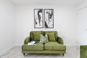 Un sofá verde con cojines estampados, una revista y dos cuadros abstractos en la pared.
