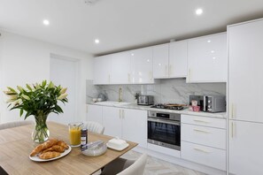 A modern kitchen with white cabinets, a marble countertop, and stainless steel appliances. - Stylish Home Near Chelsfield Station Free Wifi (Orpington)