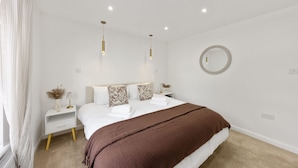 A modern bedroom with a large bed, two bedside tables, a round mirror, and pendant lights. - Stylish Home Near Chelsfield Station Free Wifi (Orpington)