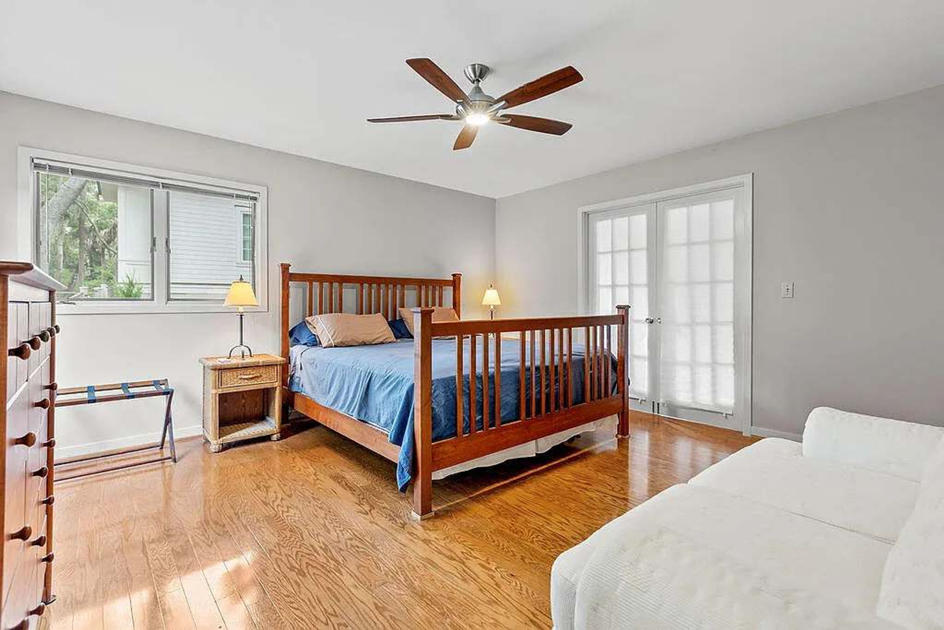 A bedroom with a wooden bed, a nightstand, a lamp, a ceiling fan, and a large window.