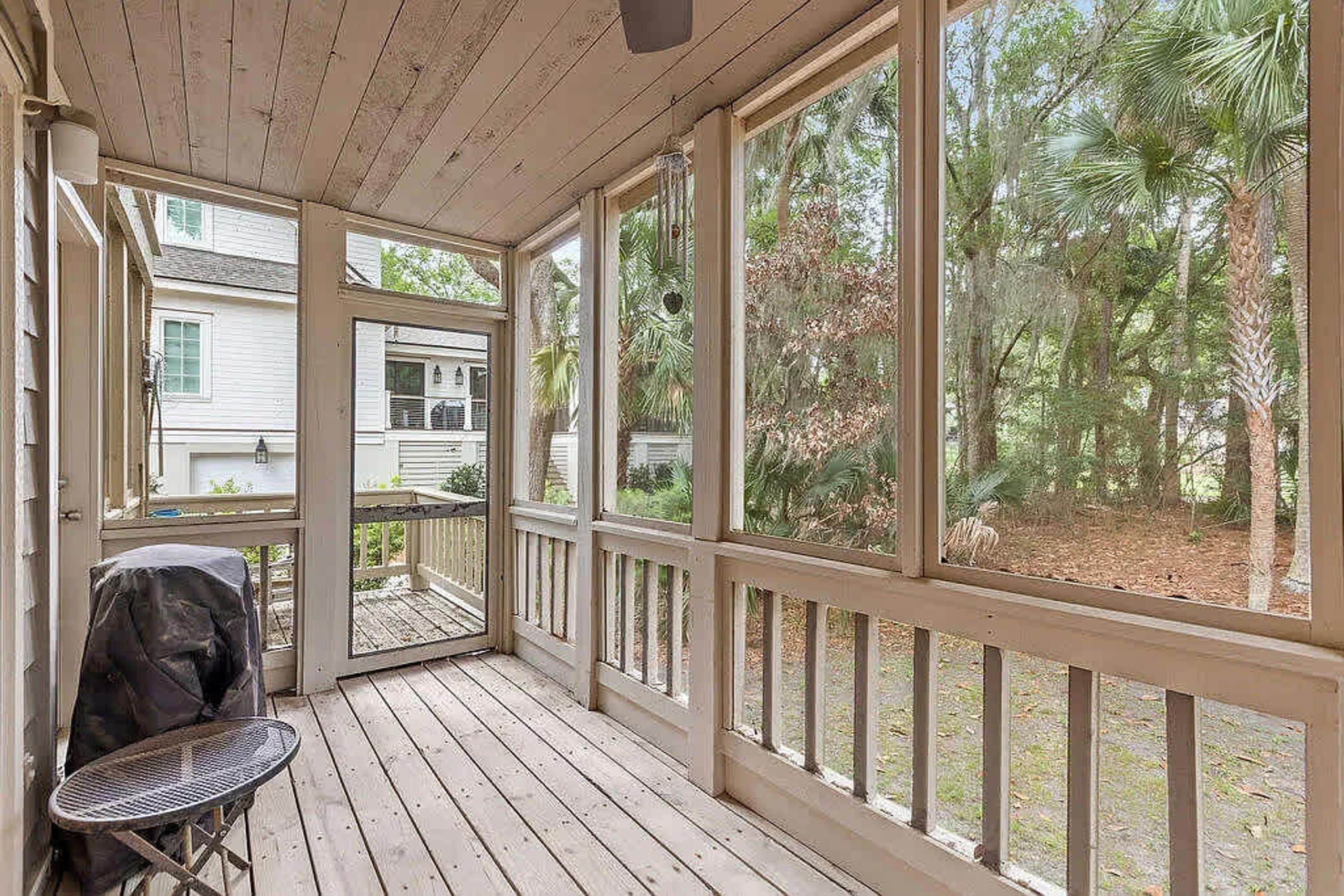 A covered porch with a table and grill, large windows, and a view of a residential area with trees.