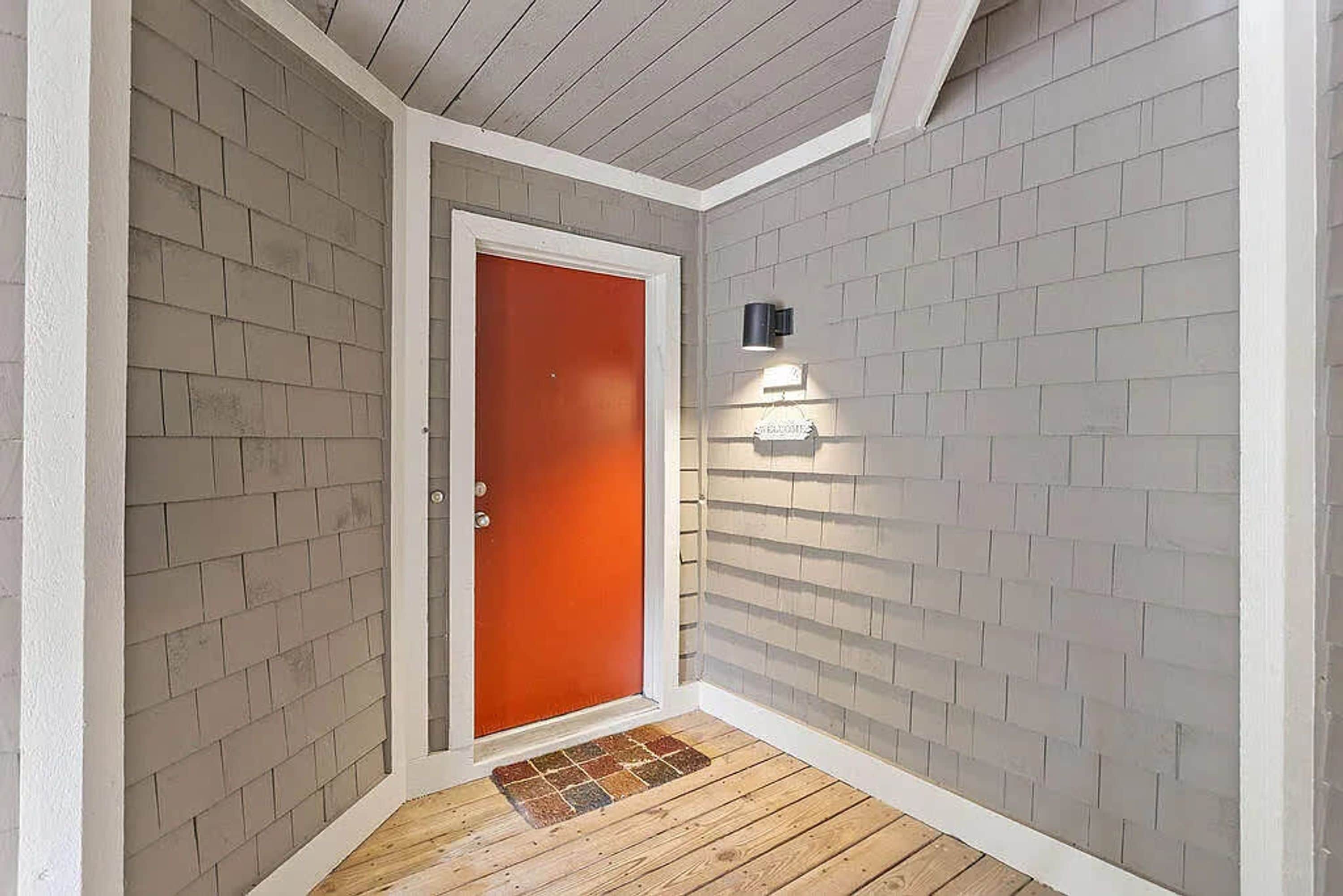 Una habitación de esquina con puerta roja, paredes blancas y suelo de madera.