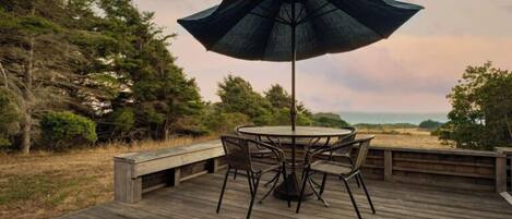 A wooden deck with a round table and chairs, an umbrella, and a view of the beach.