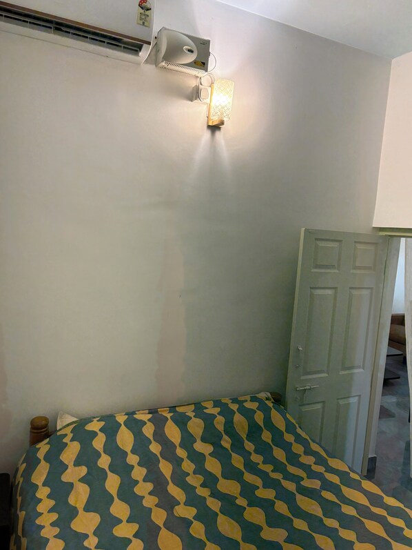 A room with a bed, a wall-mounted air conditioning unit, and a door.