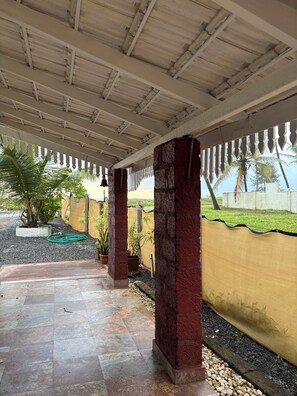 A covered outdoor area with tiled flooring, a pergola structure, and a yellow wall with a decorative edge.
