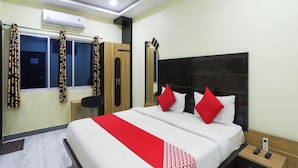 A hotel room with a bed, a bedside table, a nightstand, a wardrobe, and an air conditioning unit.