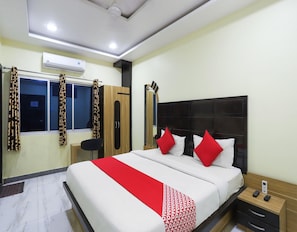A hotel room with a bed, bedside tables, a wardrobe, and an air conditioning unit. - Classic Akhand Param (Begusarai)