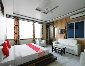 A hotel room with a bed, a sofa, a coffee table, and a TV. - Classic Akhand Param (Begusarai)