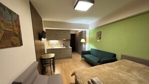 A compact hotel room with a bed, a sofa, a small dining table, and a kitchenette.
