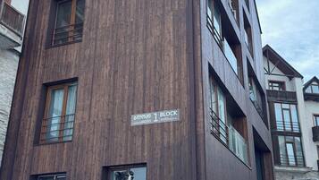 Monikerroksinen rakennus, jonka julkisivu on tehty puusta. Rakennuksen edessä on kyltti, jossa lukee ”1 Block”, ja sen edessä istuu koira.