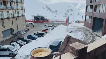 En balkong med en kaffekopp, en snötäckt parkeringsplats och byggnader i bakgrunden.