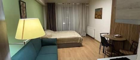 A compact hotel room with a sofa, a small dining table, a bed, and a kitchenette.
