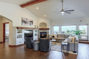 A spacious living room with a fireplace, a ceiling fan, and a large window offering a view of the outdoors. - Stunning Views! Private Home & Apartment Retreat (Colorado Springs)