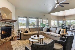 A modern living room with a fireplace, a sectional sofa, a coffee table, and a dining area with a view of mountains. - Stunning Views! Private Home & Apartment Retreat (Colorado Springs)