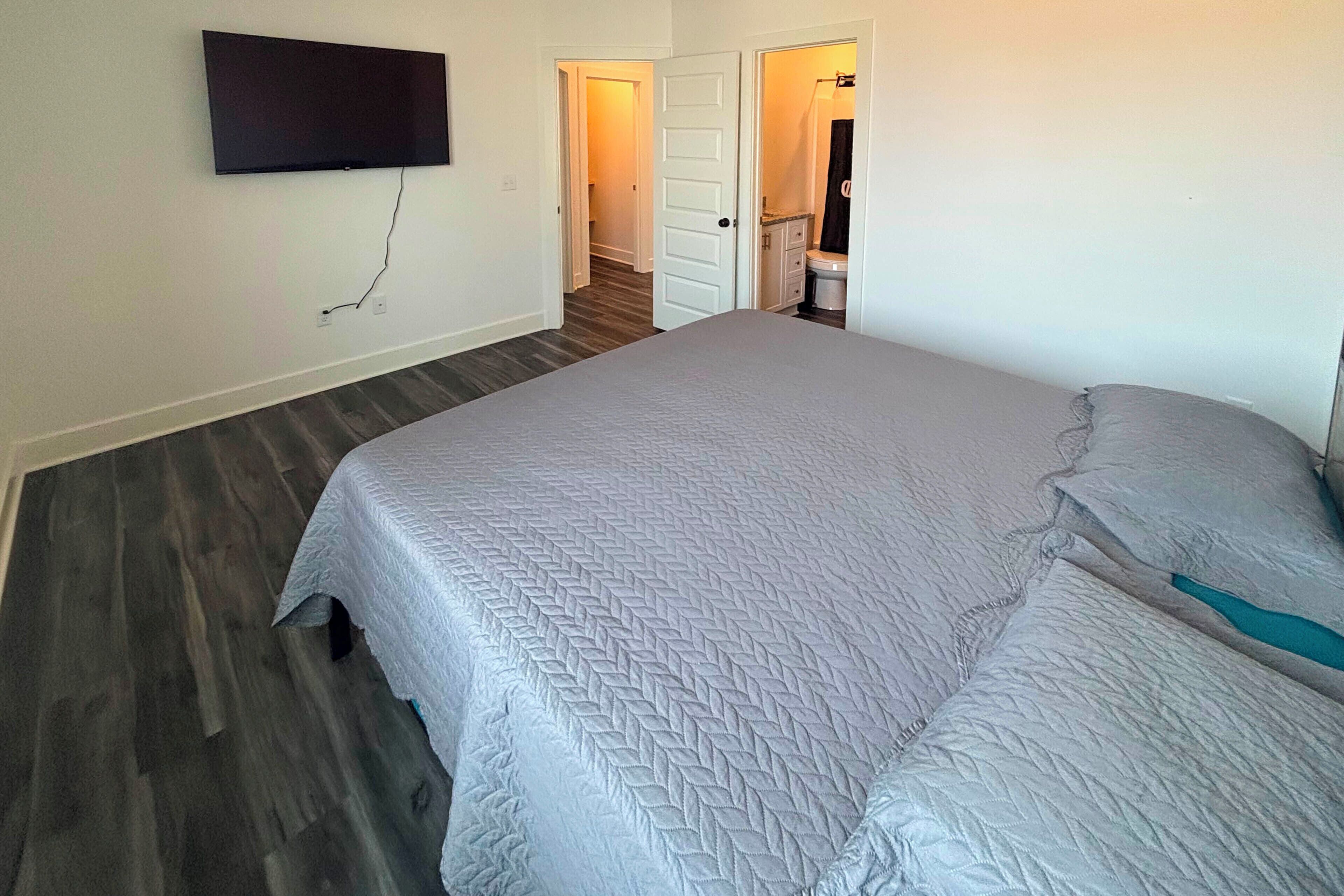 Une chambre à coucher comprenant un lit, un téléviseur à écran plat fixé au mur et une porte donnant accès à une salle de bain.