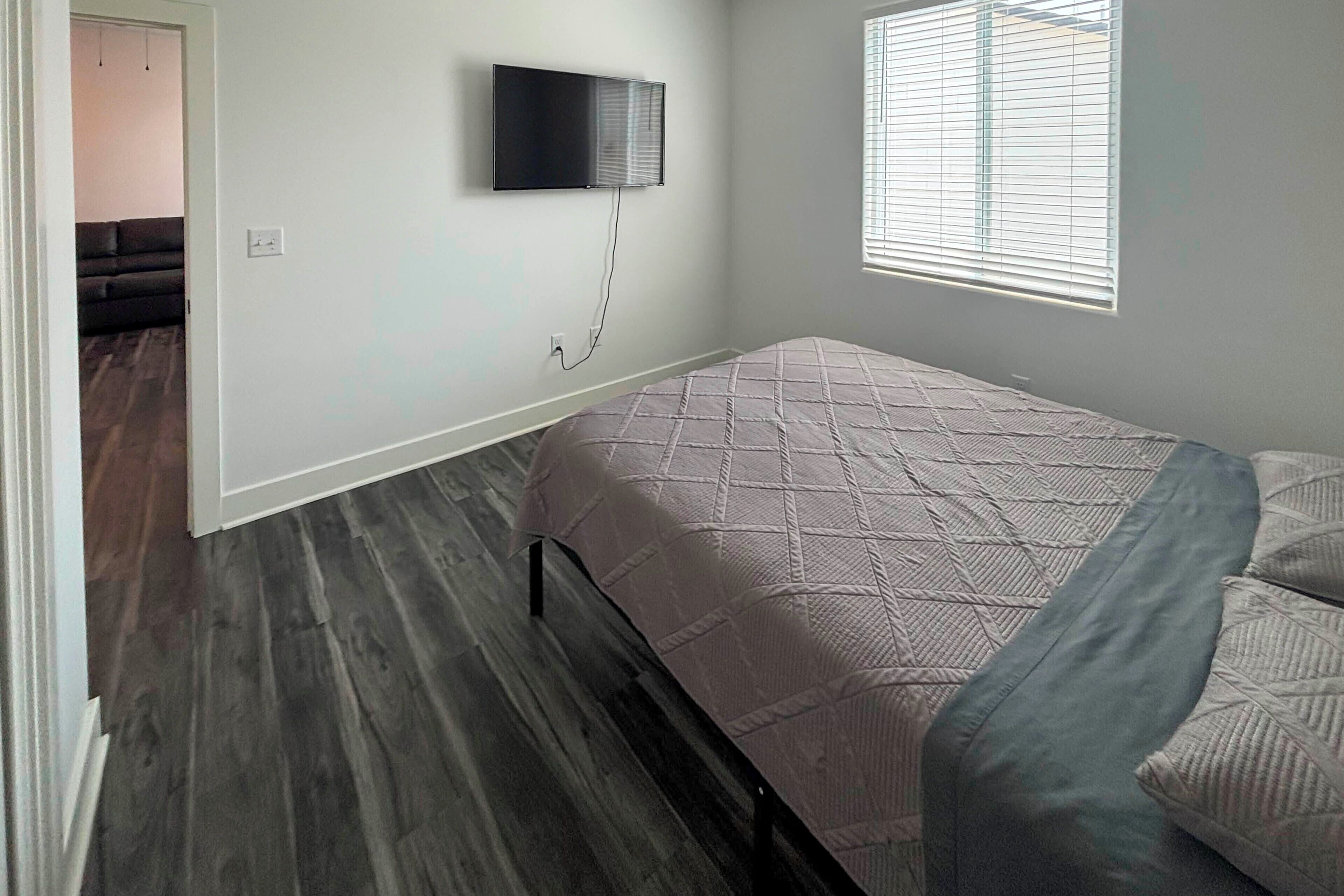 Een slaapkamer met een bed, een aan de muur bevestigde televisie en een raam met zonwering.