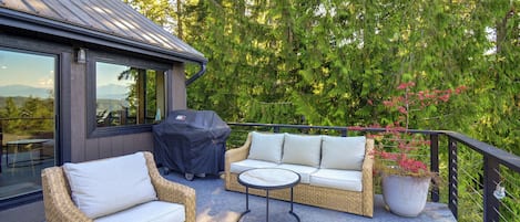 A covered outdoor seating area with wicker furniture and a barbecue grill.