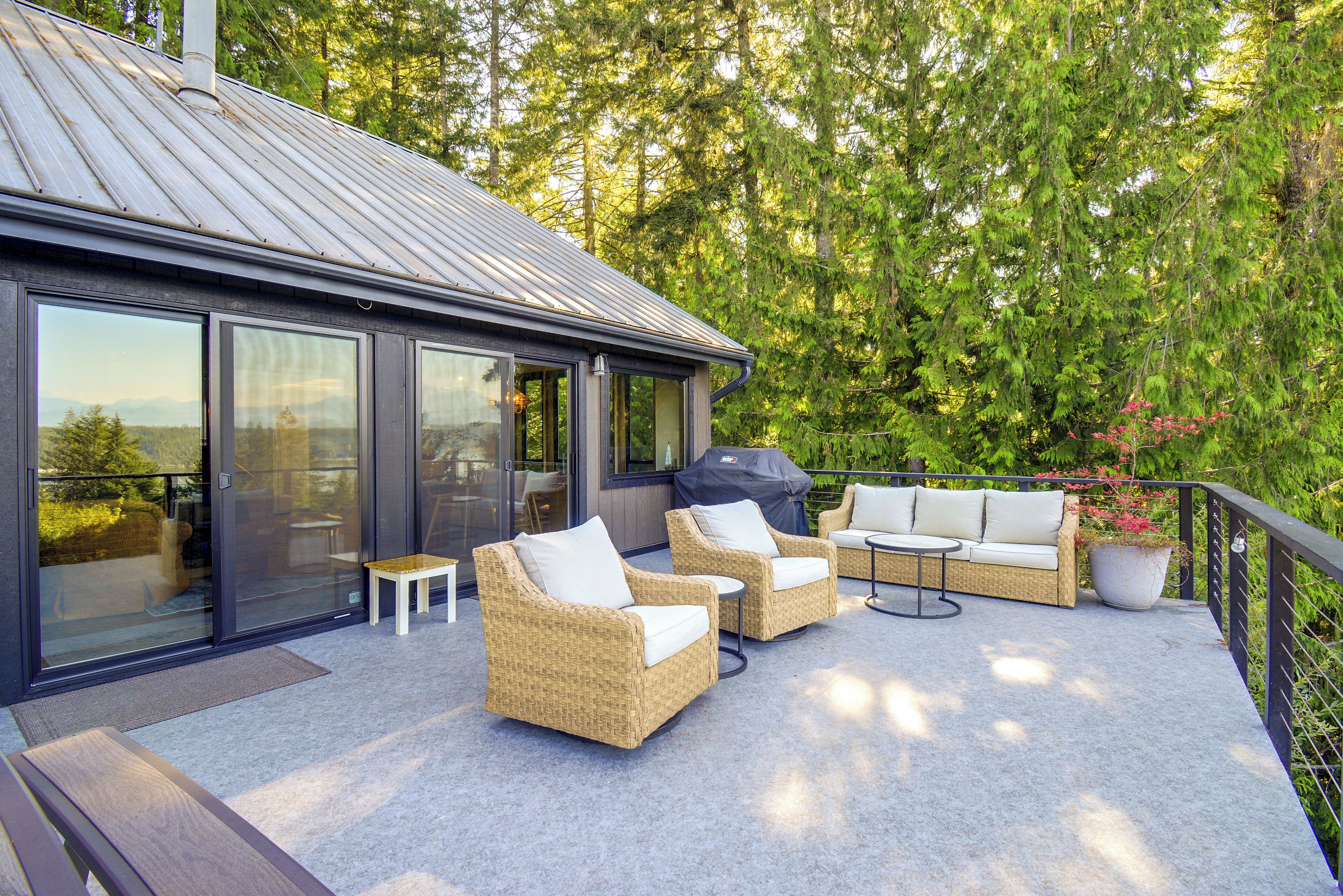 An outdoor patio with wicker furniture, a grill, and a view of a forest.