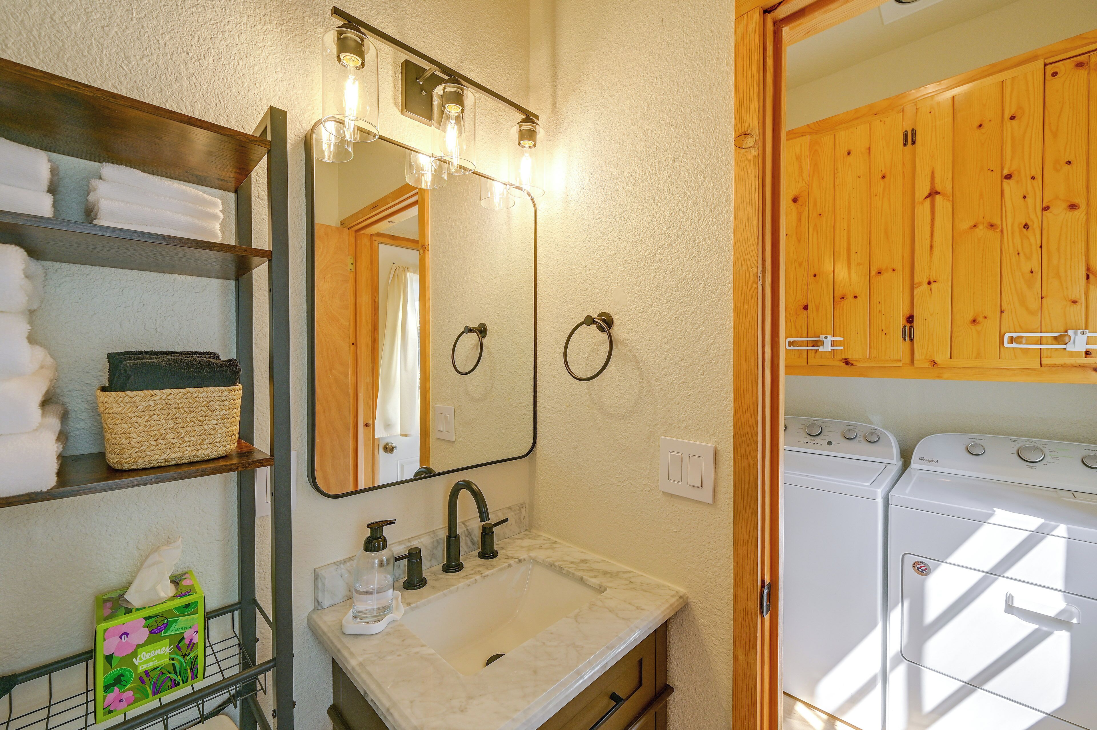 A bathroom with a sink, mirror, towel rack, and a washing machine.