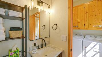 A bathroom with a sink, mirror, towel rack, and a washing machine.