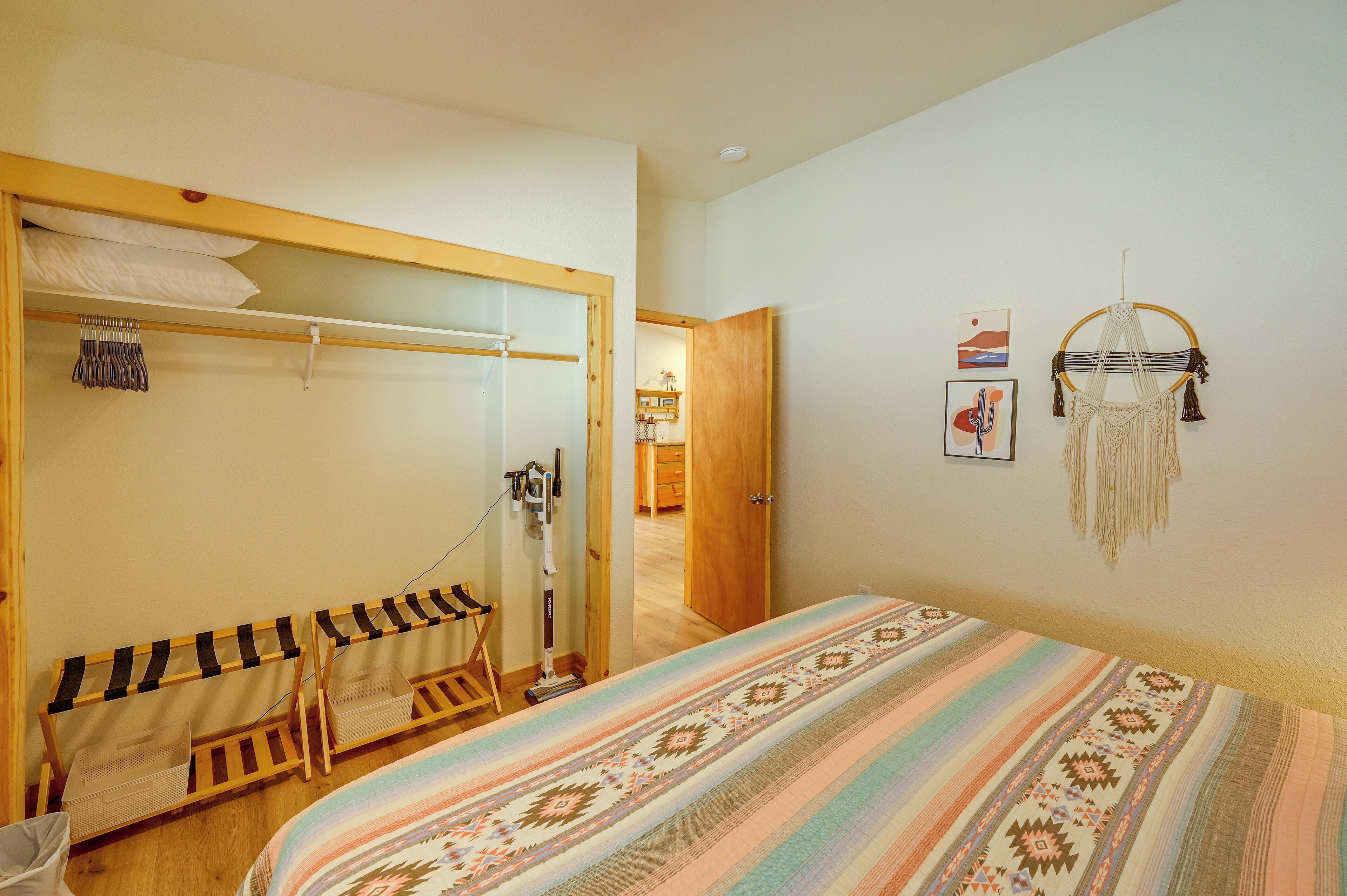 A bedroom with a bed, a wooden wardrobe, a mirror, a wall-mounted shelf, and a door leading to another room.
