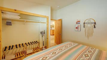 A bedroom with a bed, a wooden wardrobe, a mirror, a wall-mounted shelf, and a door leading to another room.