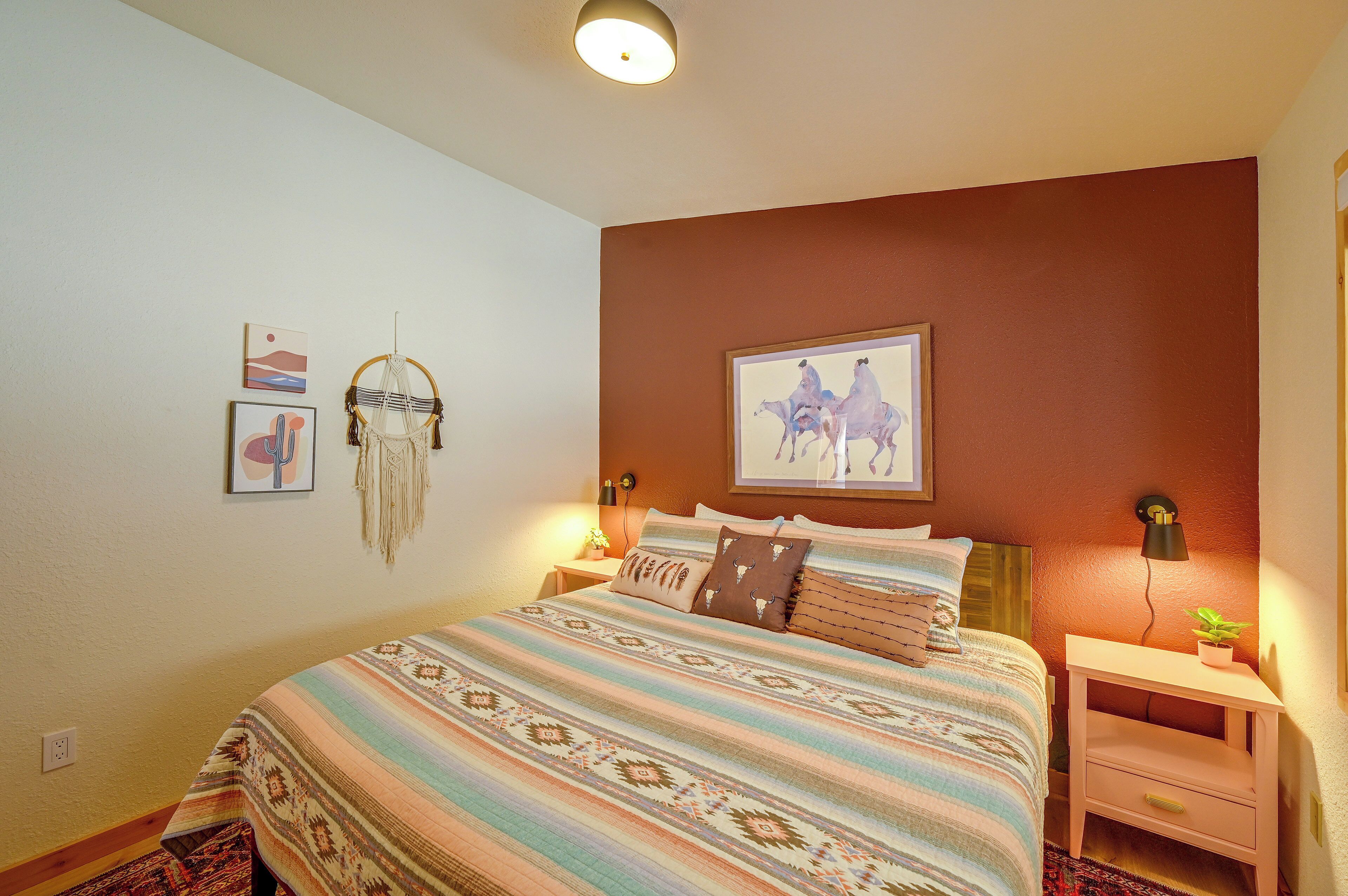 Une chambre à coucher avec un lit, des tables de chevet, une lampe fixée au mur et un tableau encadré.