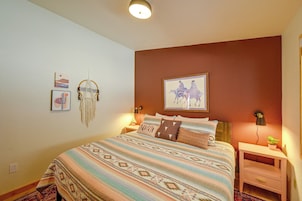 A bedroom with a bed, bedside tables, a wall-mounted lamp, and a framed picture.