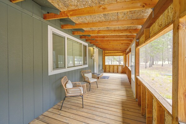 A covered porch with wooden beams, a window, and two wicker chairs.